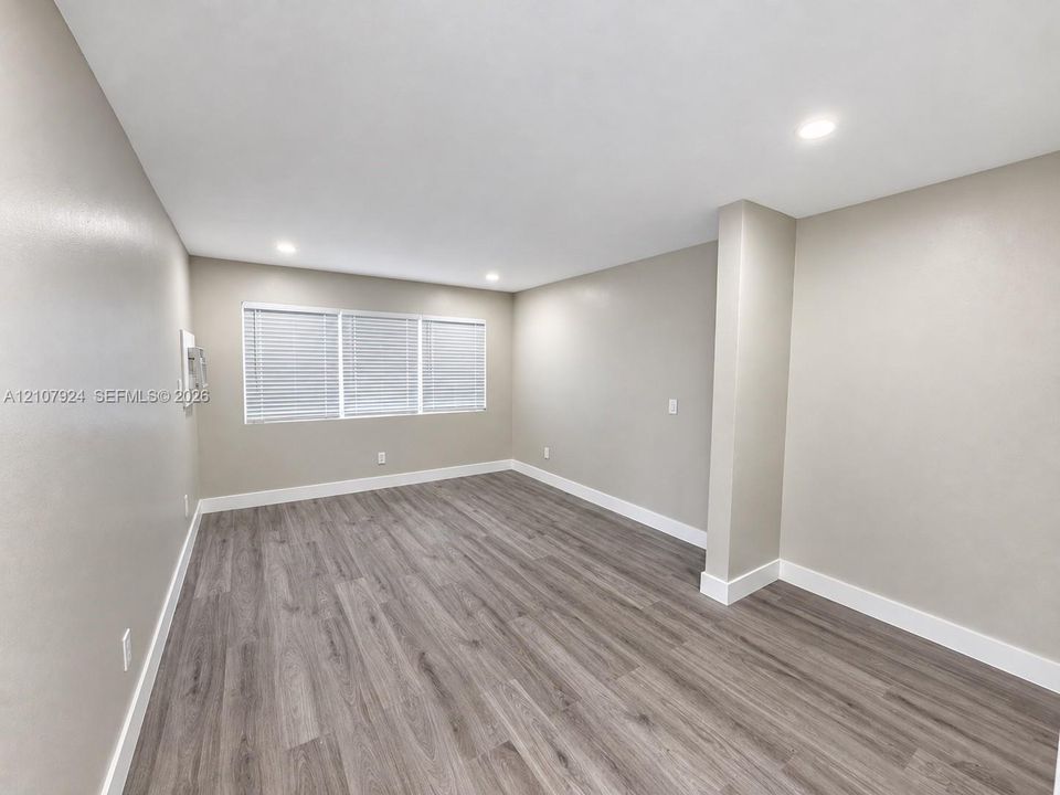 Neutral-toned interior room featuring wood-finish flooring, recessed lighting, and a window with integrated blinds