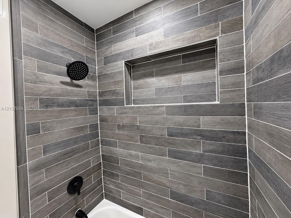 Walk-in shower enclosure featuring wood-finish tile wall cladding, matte black rainfall showerhead, integrated wall niche, and matte black plumbing fixtures