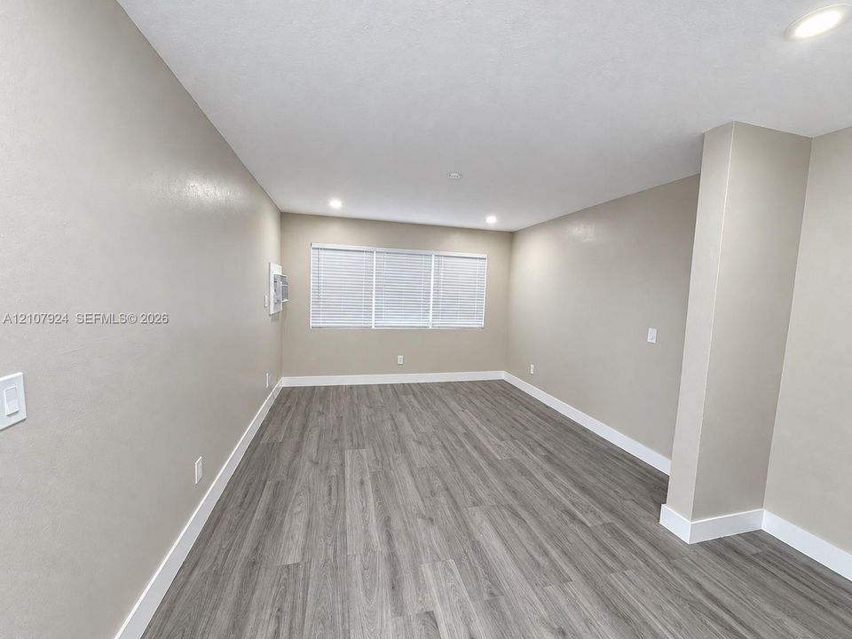 Neutral-toned interior space featuring wood-finish flooring, recessed lighting, and a triple-pane window with installed blinds