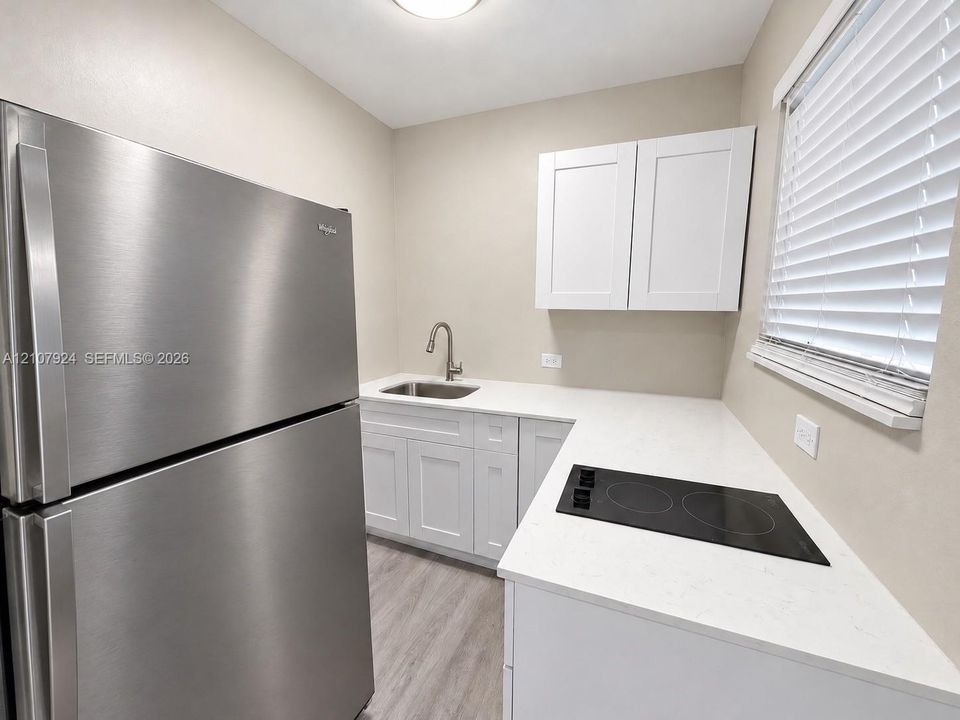 Kitchen featuring white cabinetry, solid surface countertops, a stainless steel refrigerator, a built-in cooktop, and a stainless steel undermount sink with a gooseneck faucet