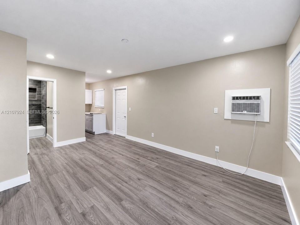 Wood-finish flooring, neutral wall tones, recessed lighting, and a wall-mounted climate control unit