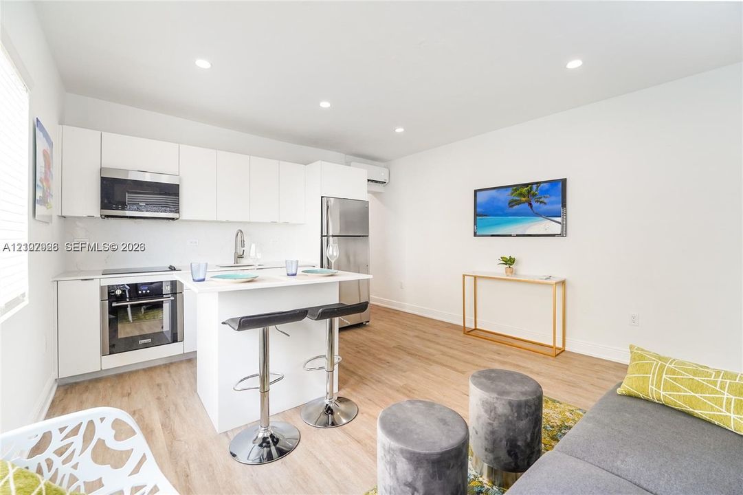 Open-concept kitchen featuring white flat-panel cabinetry, stainless steel appliances, a central island, and wood-finish flooring