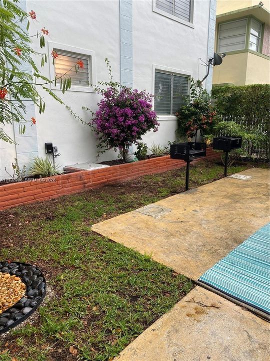 Concrete patio area featuring two permanent charcoal grills, a decorative masonry retaining wall, and landscaped planting beds