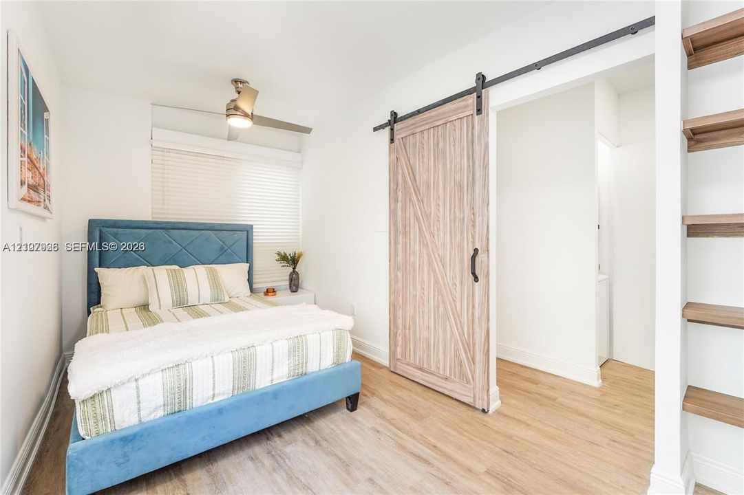 Wood-finish flooring, sliding barn door with black hardware, built-in wooden shelving, and ceiling-mounted light fixture
