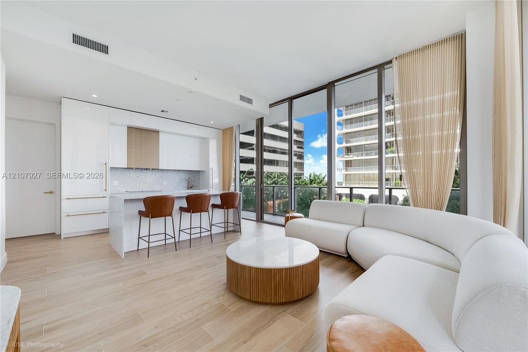 Open-concept living space featuring wood-finish flooring, floor-to-ceiling windows, and a modern kitchen with a stone-top island, gloss-finish cabinetry, and built-in appliances
