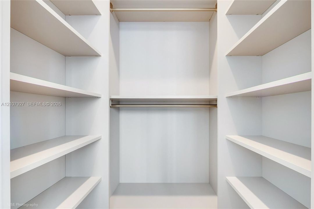 Custom closet featuring white built-in shelving and dual horizontal metal hanging rods
