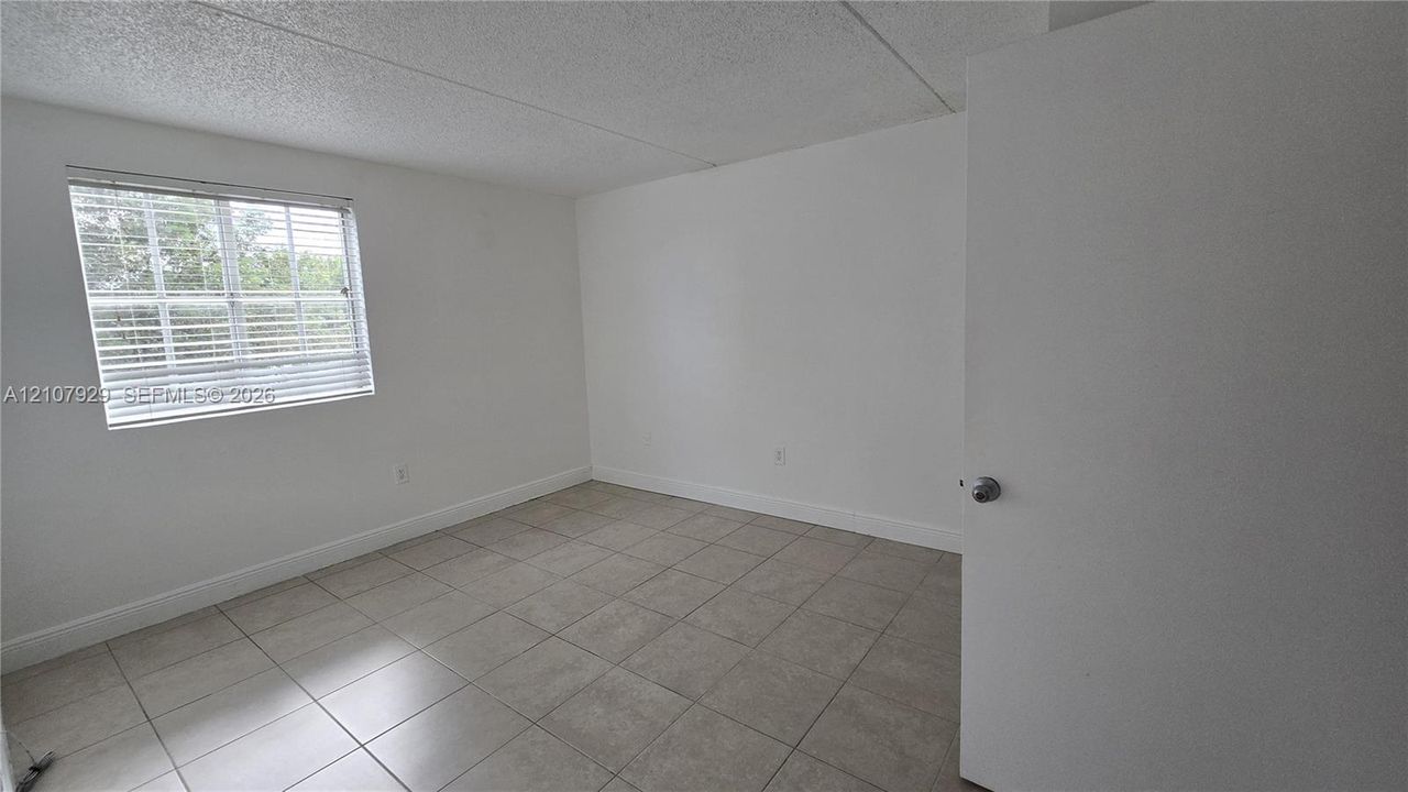 Neutral-toned tile flooring, white interior walls, and a single-pane window with installed horizontal blinds