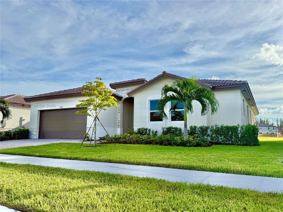 Single-story exterior featuring a tile roof, light-toned stucco facade, stone masonry accents, multi-car garage, and manicured landscaping