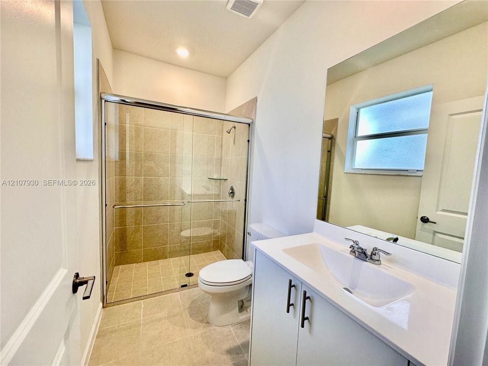Bathroom featuring a glass-enclosed shower with tile surround, a white vanity with a composite countertop and integrated basin, a large wall-mounted mirror, and tile flooring