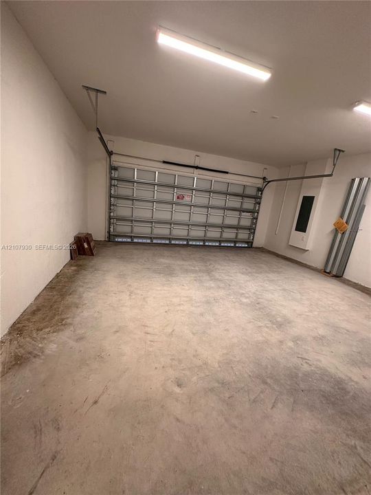 Multi-car garage featuring a sectional overhead door, finished walls, concrete flooring, and ceiling-mounted fluorescent lighting