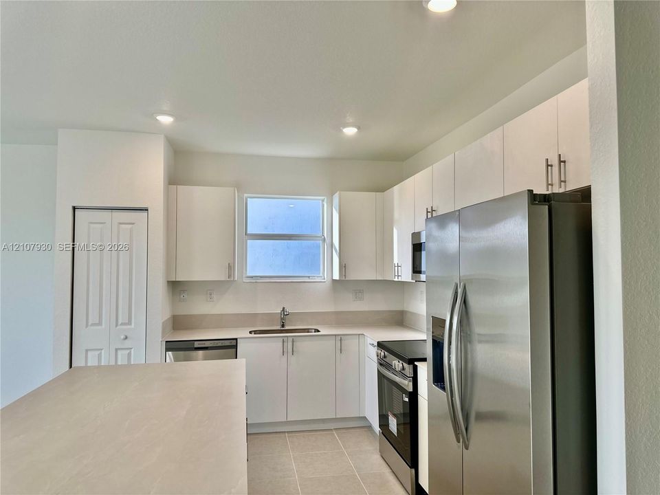 Kitchen featuring white flat-panel cabinetry, stainless steel appliances, a central island with a solid surface countertop, and tile flooring
