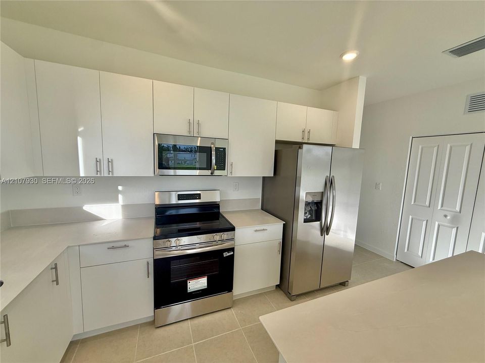Kitchen featuring flat-panel white cabinetry, stone-finish countertops, stainless steel appliances, a mounted microwave, and tile flooring