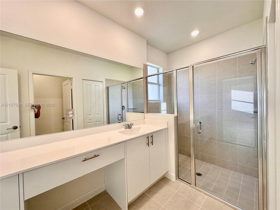 Bathroom featuring a white vanity with a solid-surface countertop, an integrated sink, full-width vanity mirror, walk-in shower with tile surround, and recessed ceiling lighting