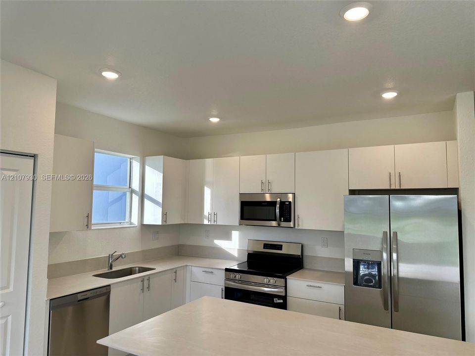 Kitchen featuring white flat-panel cabinetry, light-toned solid surface countertops, stainless steel appliances, and recessed ceiling lighting