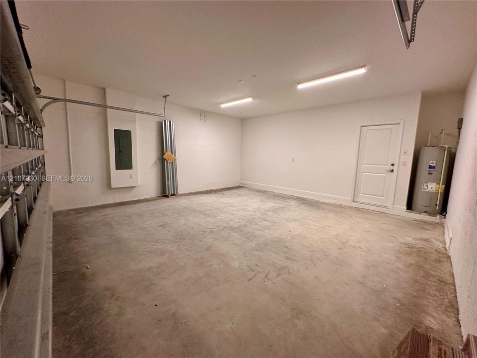 Multi-car garage featuring a concrete floor, dual linear overhead light fixtures, a paneled interior access door, and an integrated water heater