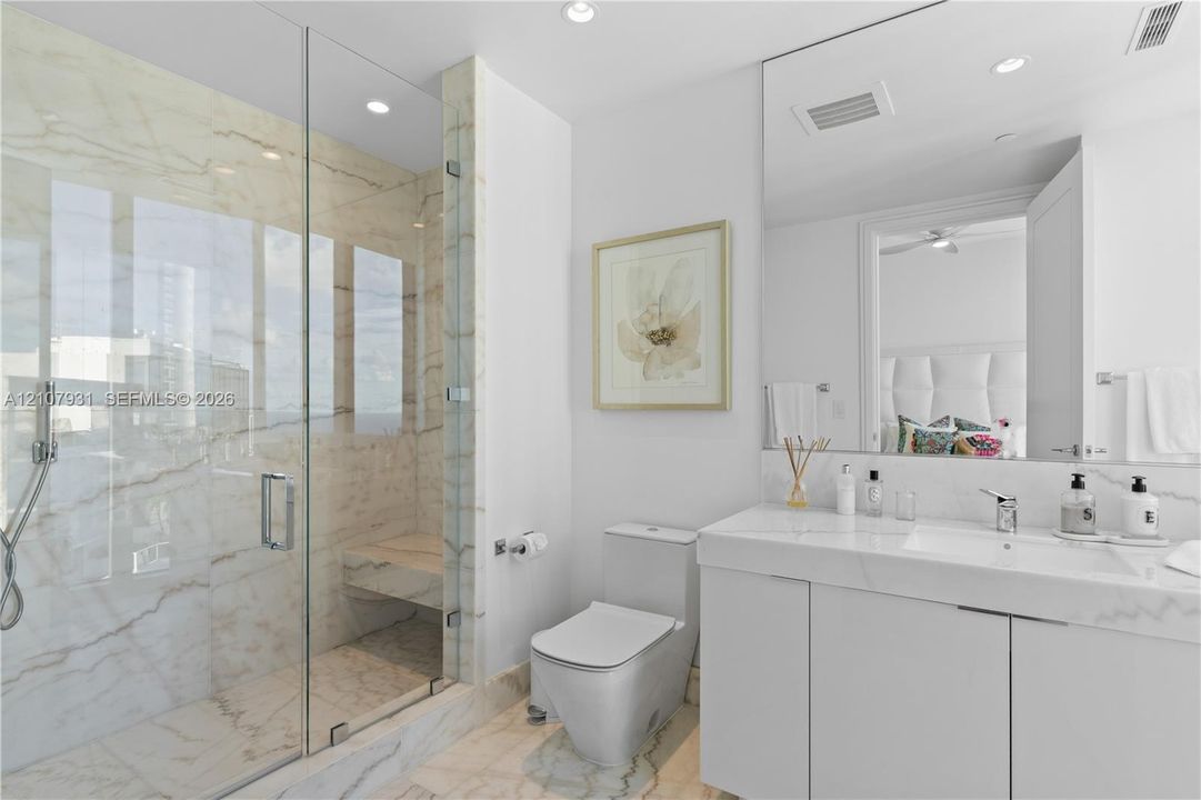 Glass-enclosed walk-in shower with stone wall surround, built-in shower bench, solid-surface vanity countertop with integrated sink, and full-width wall mirror