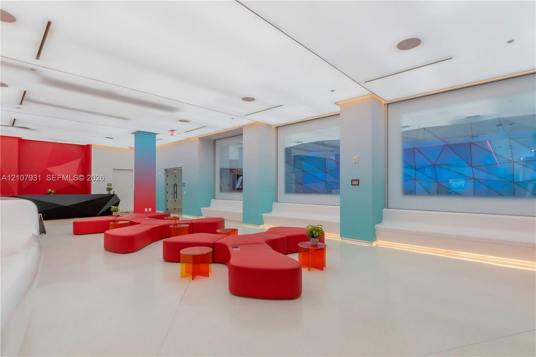 Modern interior space featuring an expansive ceiling with integrated recessed lighting, built-in tiered perimeter seating, smooth-finish flooring, and structural columns with gradient coloring