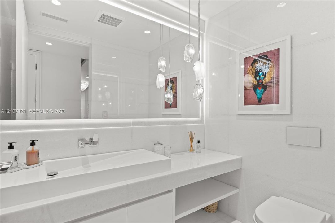 Floating vanity with an integrated basin, expansive wall-to-wall mirror, tiered glass pendant lighting, and recessed ceiling illumination