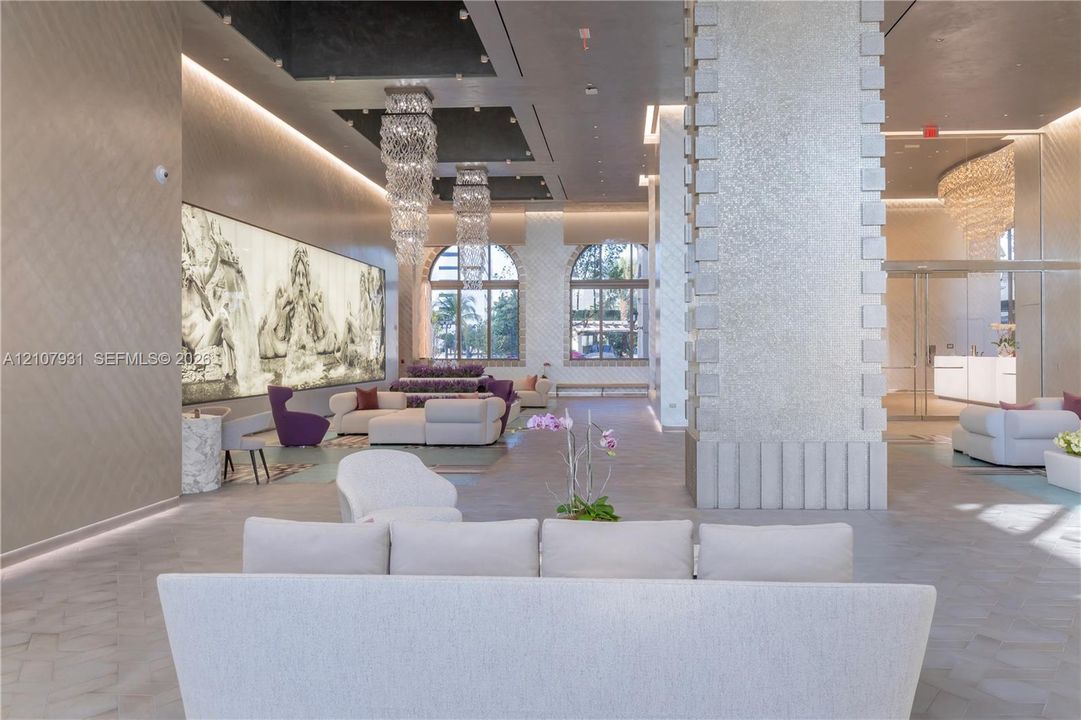 Grand lobby featuring a high-contrast coffered ceiling, tiered crystal chandeliers, stone-clad structural columns, arched windows, and large-scale backlit wall art