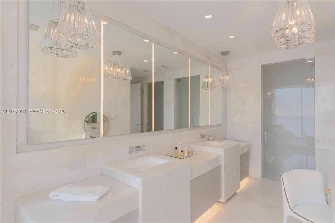 Double vanity featuring integrated rectangular sinks, stone countertops, full-width mirror with vertical LED lighting, recessed ceiling lighting, and pendant fixtures
