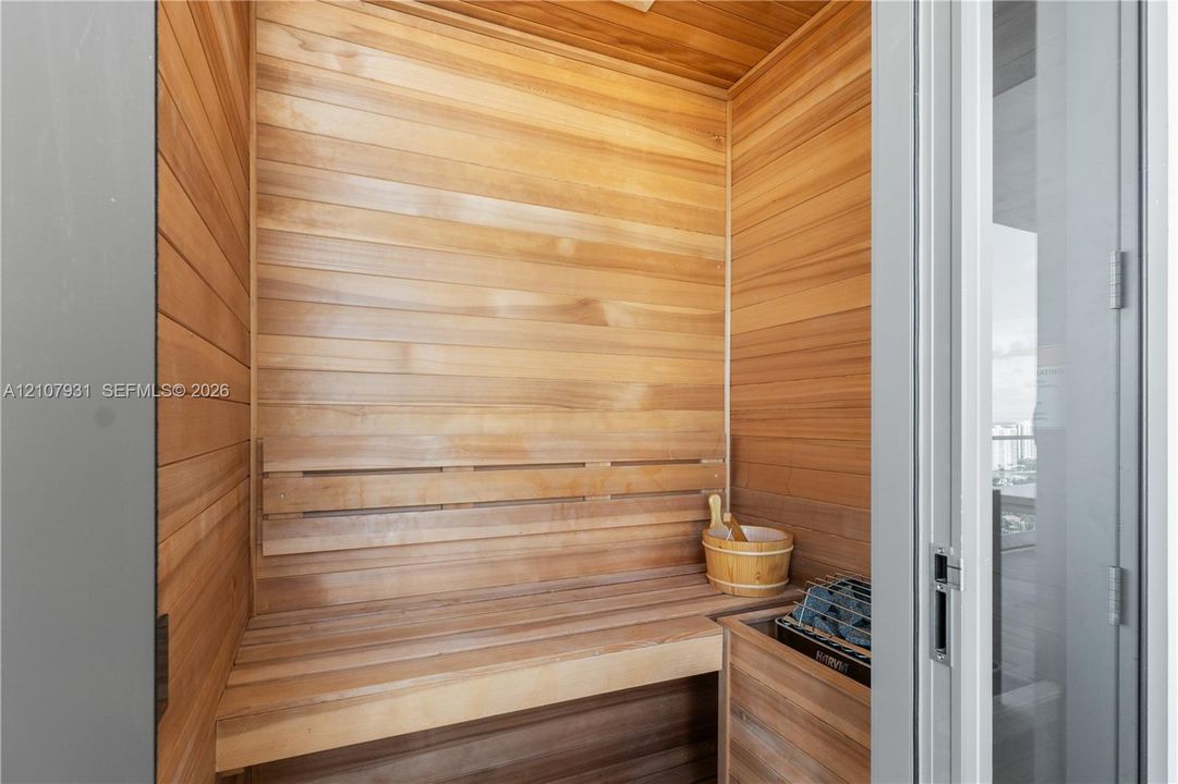 Custom sauna featuring natural wood wall paneling, tiered wood-finish bench seating, and an integrated heating element