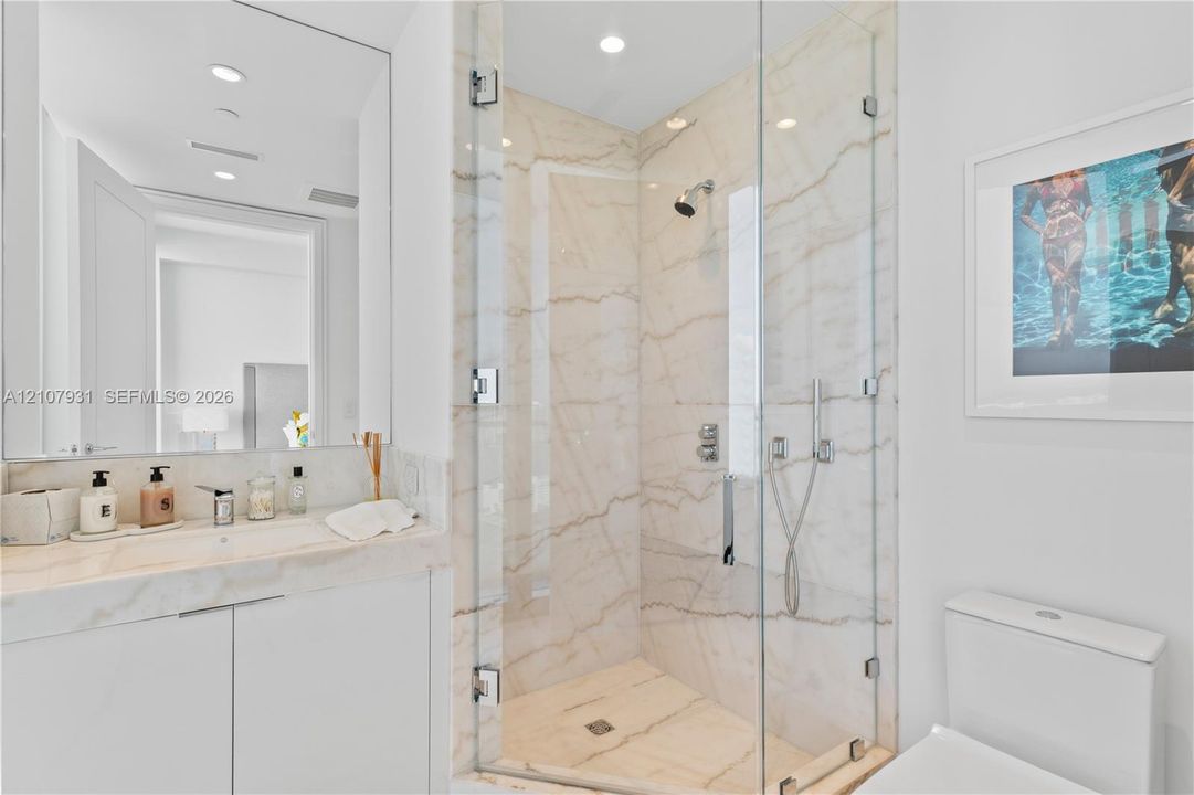 Bathroom featuring a vanity with integrated sink and stone countertop, frameless glass-enclosed shower with stone-surround, wall-to-wall mirror, and recessed lighting
