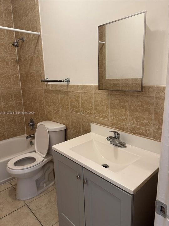 Bathroom featuring a gray vanity with an integrated basin, chrome faucet, wall-mounted medicine cabinet, and tan tiled tub surround