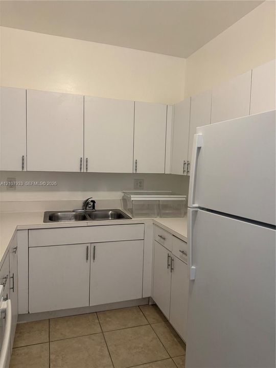 Kitchen featuring white cabinetry, solid-surface countertops, a double-basin stainless steel sink with a high-arch faucet, and tile flooring