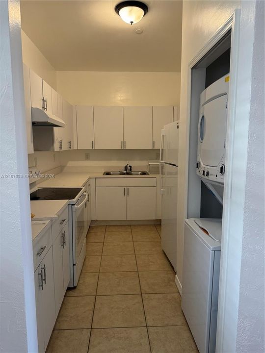 Kitchen featuring white cabinetry with metallic hardware, solid surface countertops, dual-basin stainless steel sink, tile flooring, and integrated laundry closet