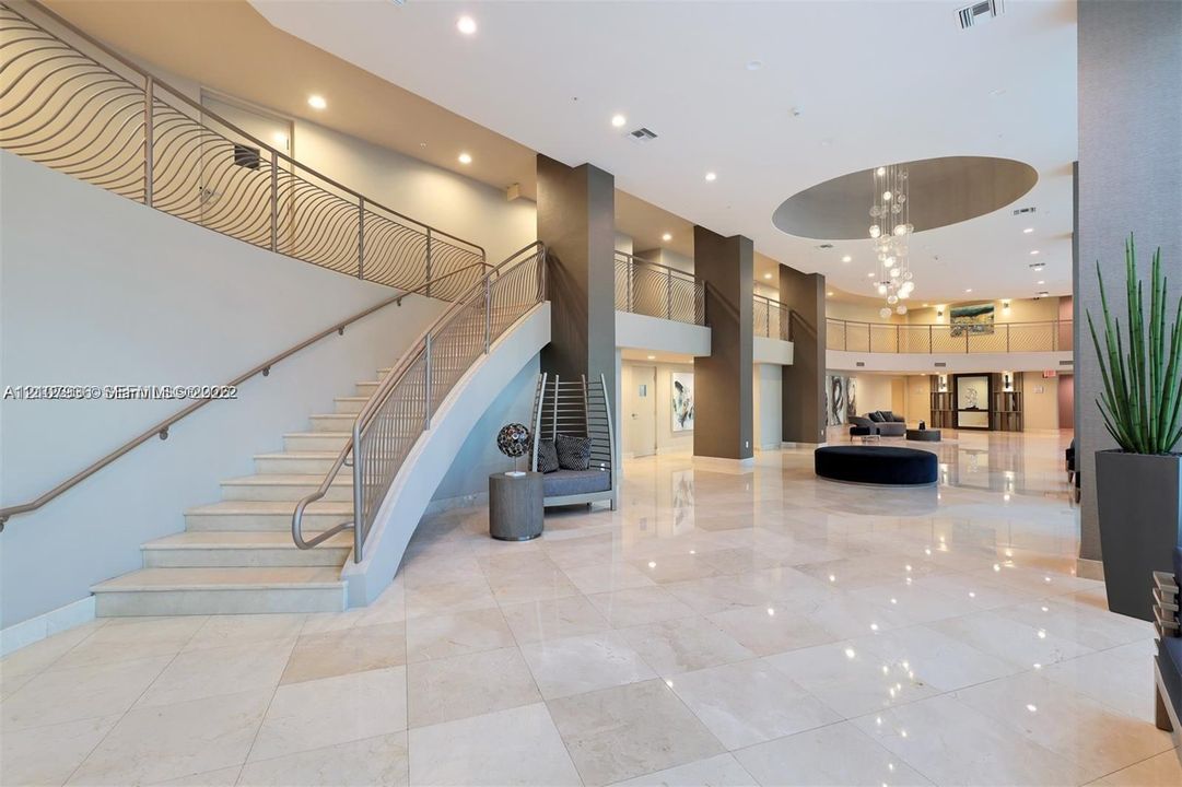 Grand lobby featuring polished stone flooring, a sweeping staircase with custom metal railings, soaring ceilings with recessed lighting, and a multi-tiered crystal chandelier