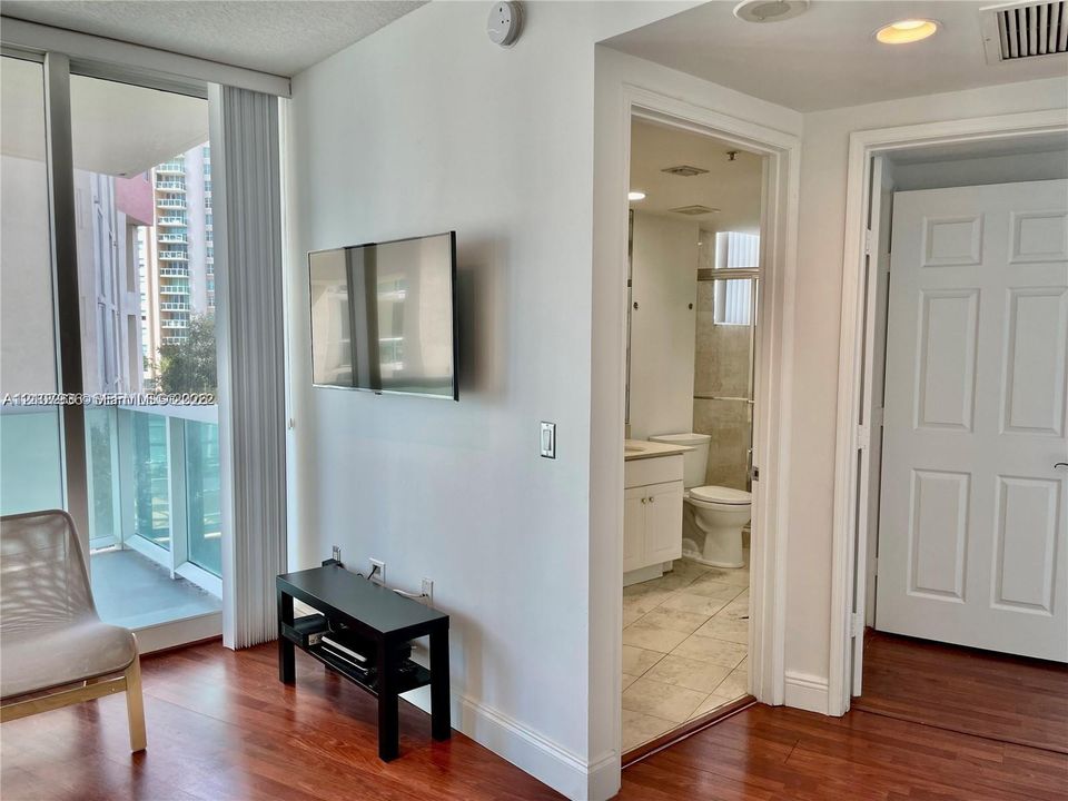 Floor-to-ceiling glass paneling with sliding door access to a private balcony, wood-finish flooring, and white paneled interior doors