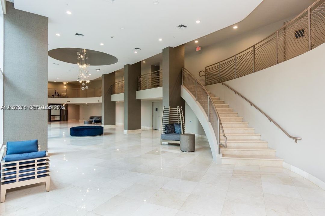 Expansive multi-level lobby featuring polished stone flooring, a curved staircase with metal railings, recessed ceiling lighting, and a decorative circular ceiling inlay with integrated light fixture