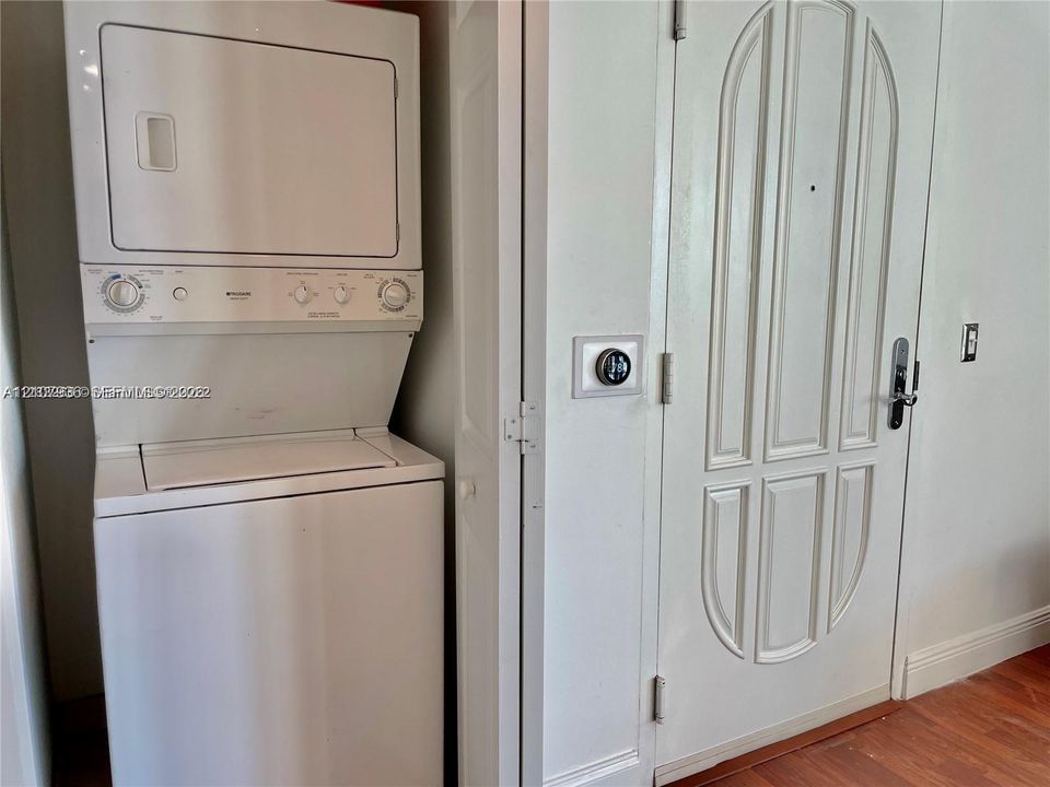 Stacked white laundry unit, wall-mounted smart thermostat, and six-panel interior door with brushed metal hardware set against wood-finish flooring