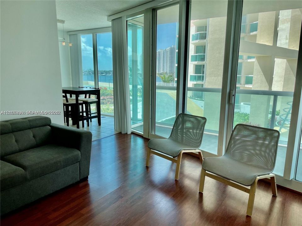 Floor-to-ceiling glass panel windows, wood-finish flooring, and access to a balcony with glass railings