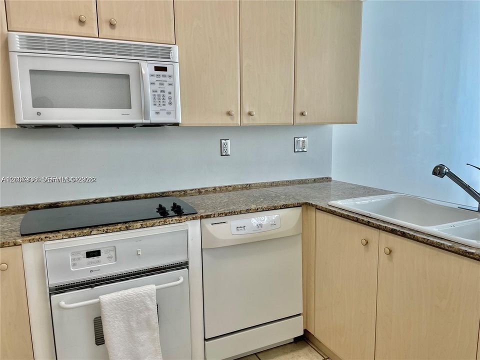 Kitchen featuring light wood-finish cabinetry, stone-surface countertops, built-in microwave, electric cooktop, and an integrated dishwasher