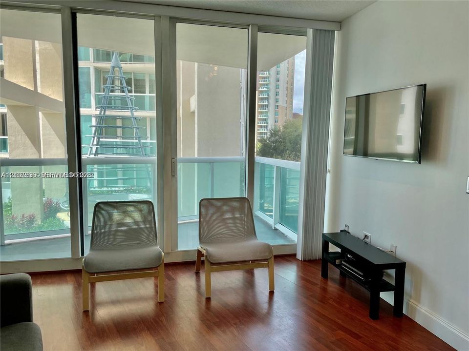Floor-to-ceiling windows, wood-finish flooring, and access to a balcony with glass railings