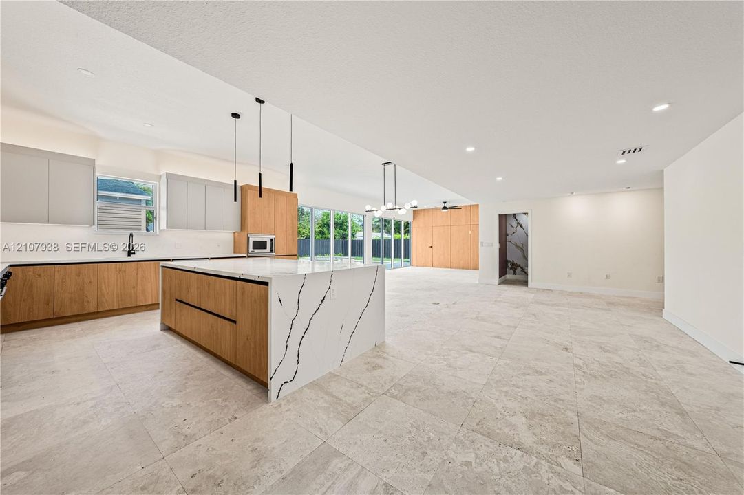 Kitchen featuring a large waterfall-edge stone island, two-tone cabinetry, stone flooring, integrated overhead lighting, and multi-panel glass doors