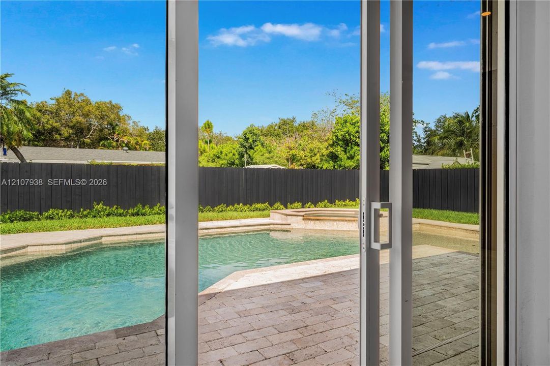 In-ground swimming pool with an integrated spa, stone paver decking, and a solid-panel privacy fence