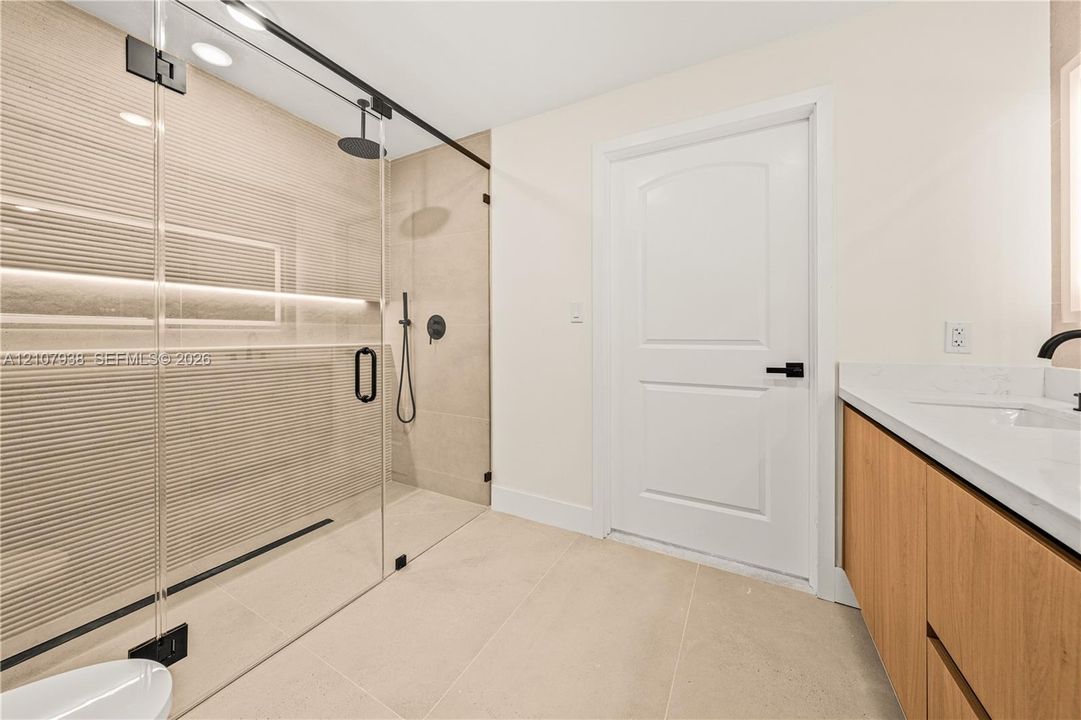 Walk-in shower featuring a glass enclosure, matte black rainfall showerhead, and a built-in recessed niche with integrated lighting