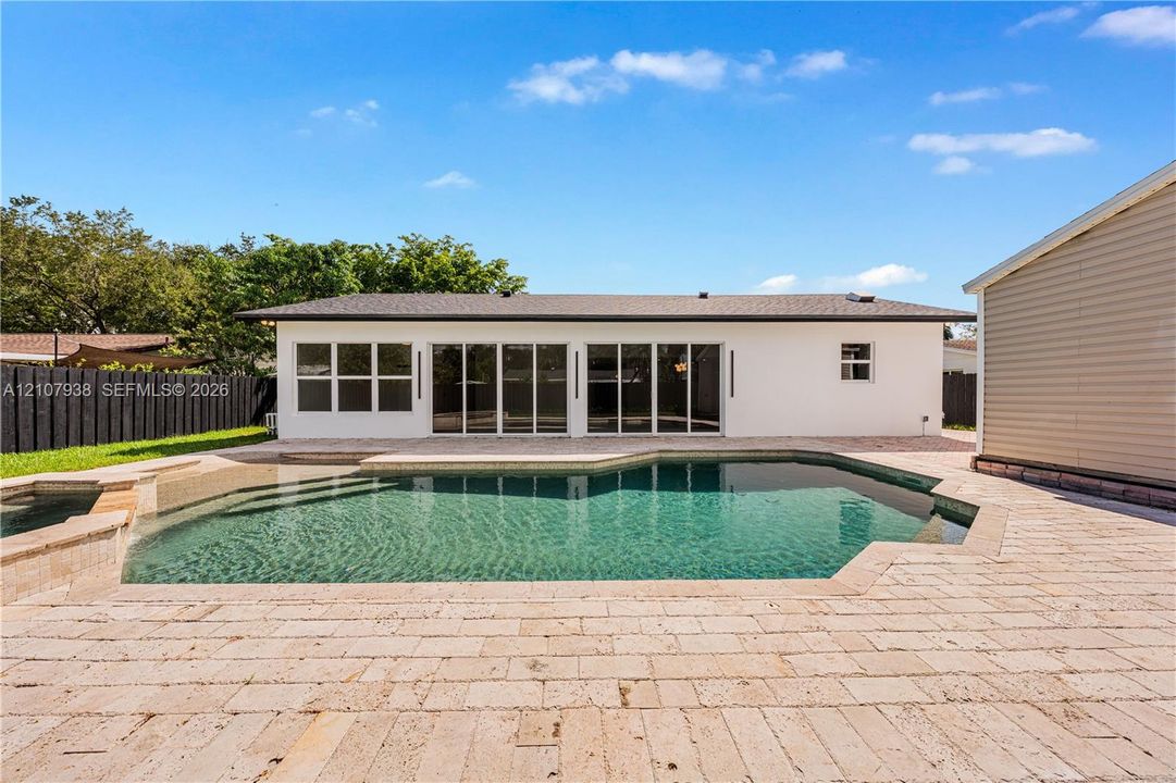 Backyard area featuring an in-ground swimming pool, integrated spa, expansive stone paver decking, and multi-panel glass sliding doors