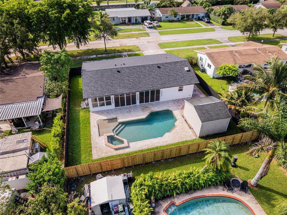 Aerial view featuring a rear-facing swimming pool, integrated spa, paved patio, detached storage structure, and fenced perimeter