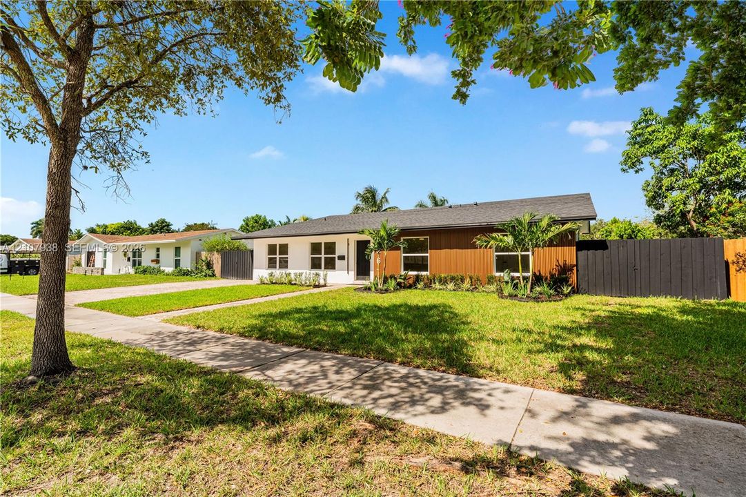 Single-story residence featuring a mid-century modern aesthetic, wood-panel siding, white stucco exterior, asphalt shingle roof, and a black privacy fence