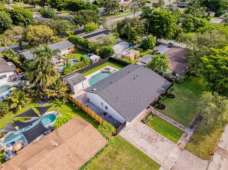 Aerial view featuring an expansive backyard, in-ground pool with integrated spa, detached storage structure, paver patio, and perimeter fencing