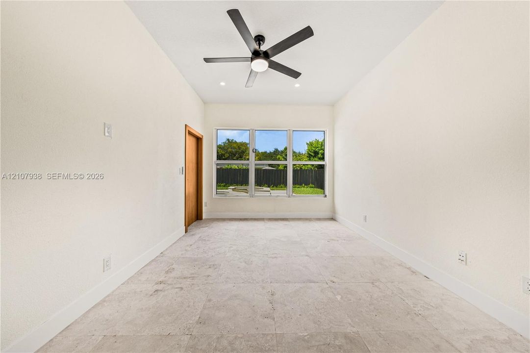 Neutral-toned stone-tile flooring, high ceilings, ceiling-mounted light fixture with matte black blades, and large multi-pane windows