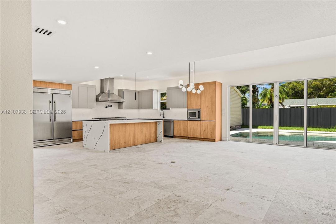 Kitchen featuring two-tone flat-panel cabinetry, a central island with waterfall-edge countertop, stainless steel appliances, recessed lighting, and large sliding glass doors opening to a pool area