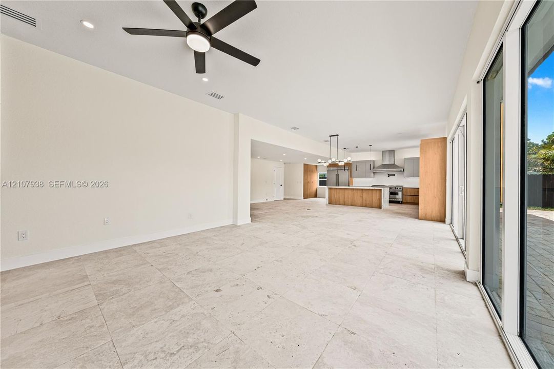 Large-format tile flooring, recessed lighting, ceiling fan with integrated light, floor-to-ceiling glass sliding doors, and kitchen featuring an island with wood-finish cabinetry