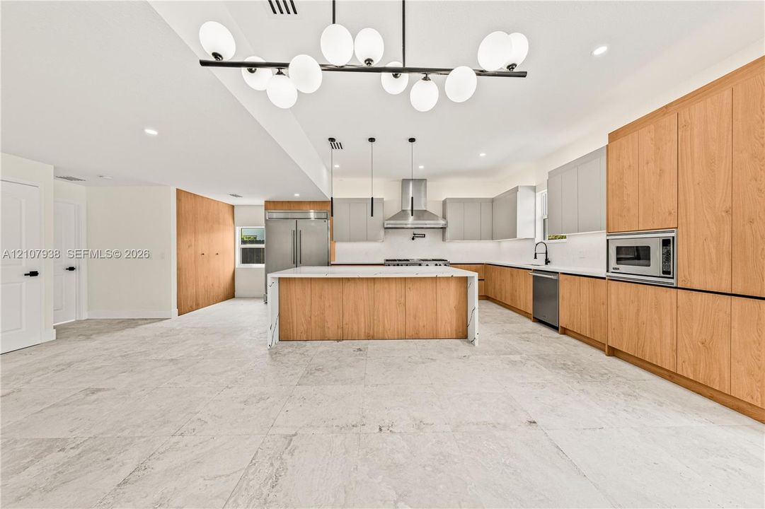 Kitchen featuring a central island with a stone-finish countertop, two-tone cabinetry with wood-finish and matte-finish panels, stainless steel appliances, and multi-light pendant fixtures