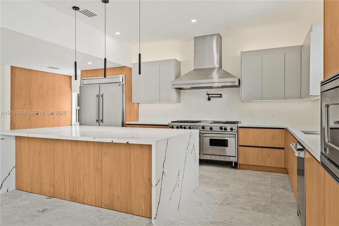 Kitchen featuring a waterfall-edge island with stone-finish countertop, dual-tone cabinetry, stainless steel professional-grade range, stainless steel chimney-style range hood, and stone-finish flooring