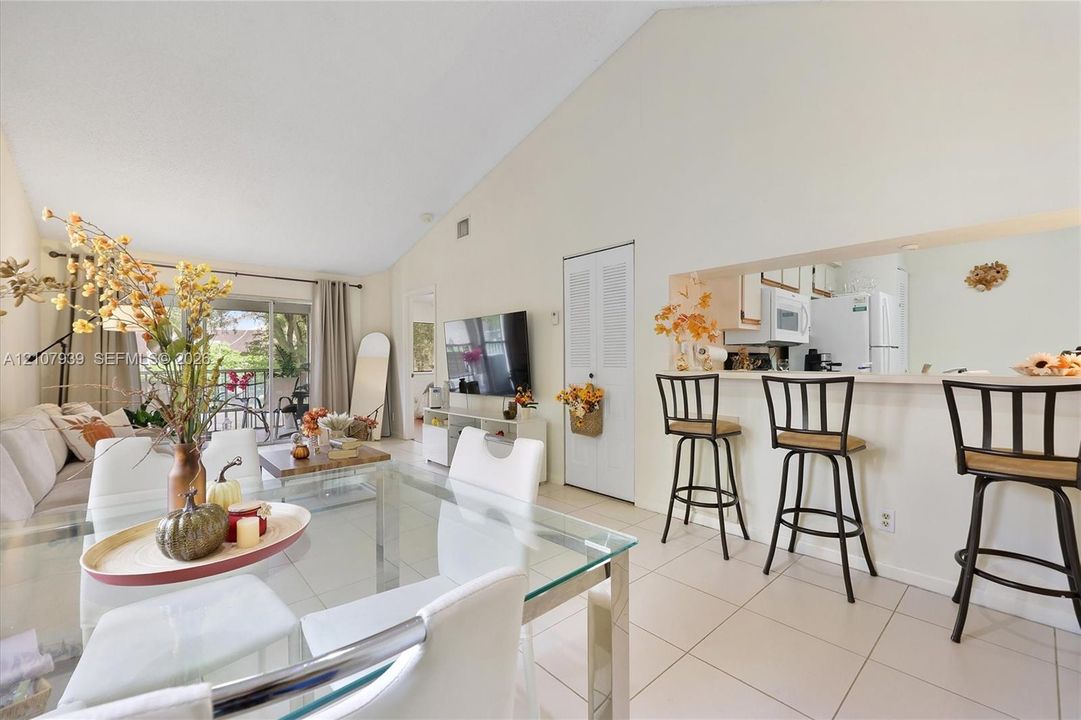 Vaulted ceiling, open-concept floor plan, tile flooring, and kitchen passthrough window with breakfast bar