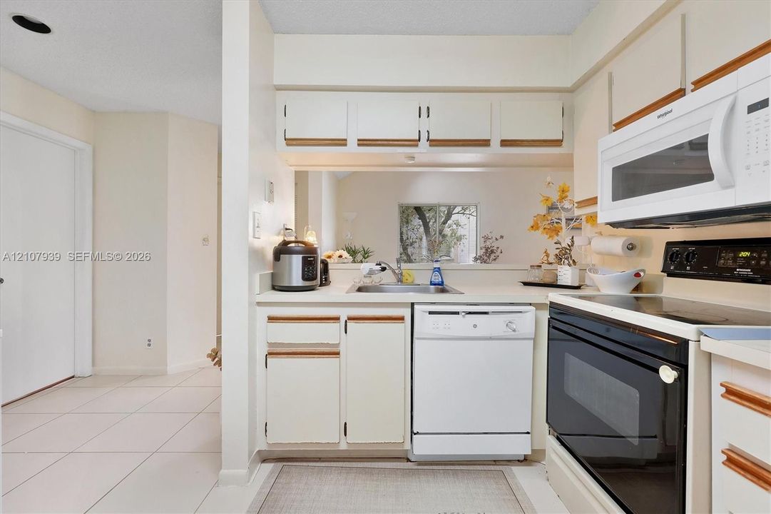 Kitchen featuring white cabinetry, integrated microwave, stainless steel sink, tile flooring, and a passthrough opening